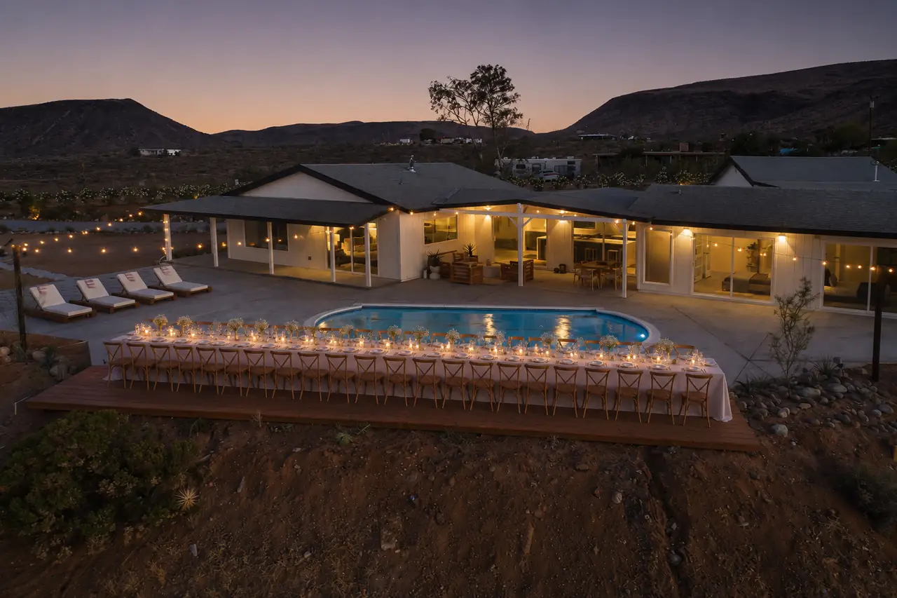 Long candlelit dinner table beside pool at dusk