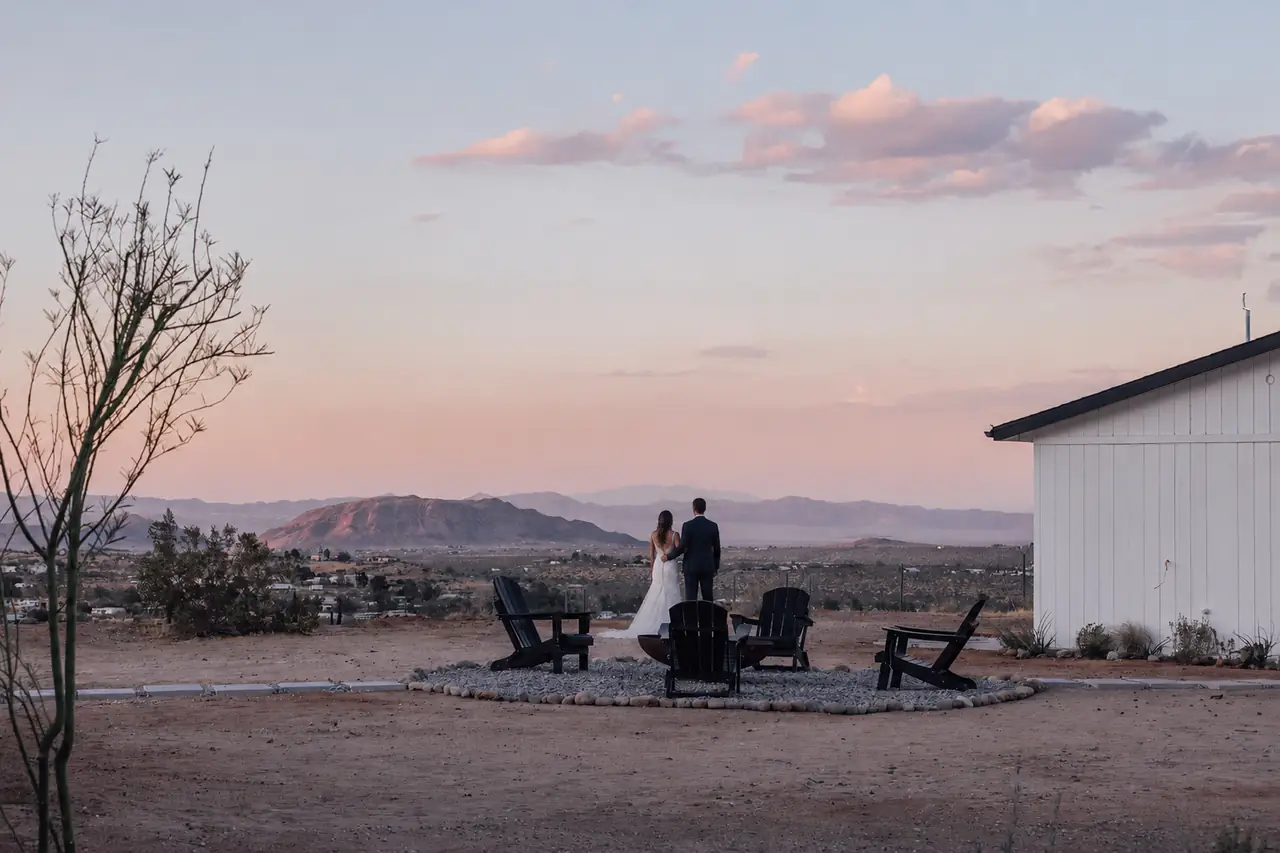 Couple standing beside the firepit with pastel sunset views across the valley